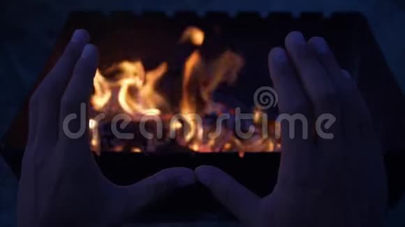 在黄昏时分温暖他的双手靠近篝火的人的慢动作手视频的预览图