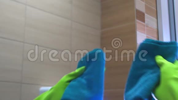 戴绿色手套的女人用蓝色微纤维布清洁浴室里的镜子视频的预览图