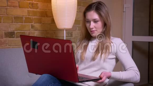 年轻有魅力的白种人深色头发的女性在笔记本电脑上看电影并被逗乐和娱乐视频的预览图