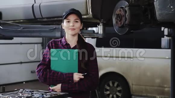 女车机械师在车的背景上戴着一顶黑色的帽子穿着一件格子衬衫带着一块平板电脑作为文件视频的预览图