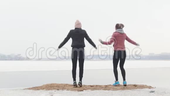 外部培训两个苗条的女人站在雪地海滩上跳跃视频的预览图