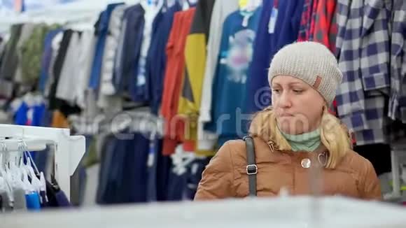 一个穿着冬衣戴着帽子的中年妇女去了一家儿童服装店在货架上视频的预览图