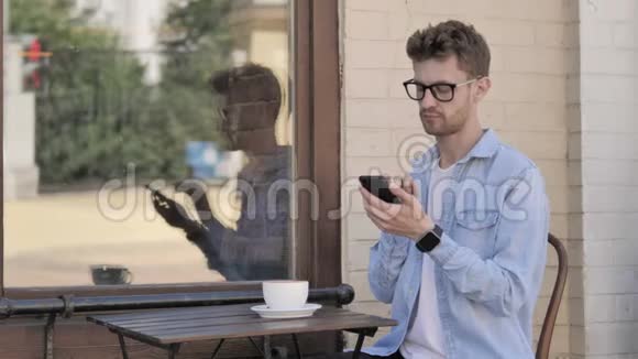 在户外咖啡厅使用智能手机和笔记本电脑的年轻人视频的预览图