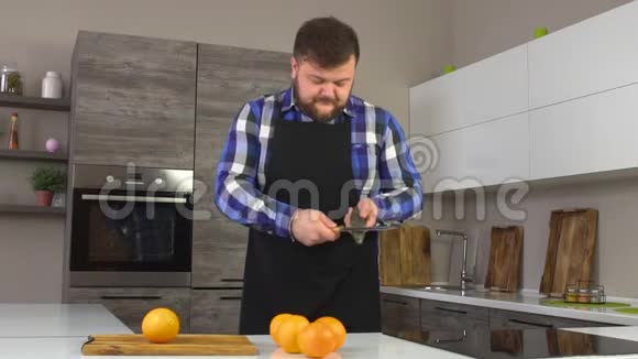 一个留着胡子的白种人正在现代化的厨房里磨一把刀桌上摆着橘子慢吞吞地说视频的预览图