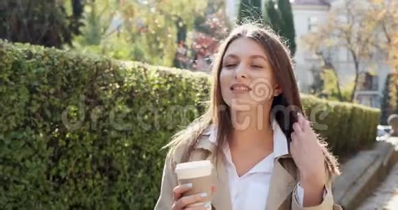 年轻迷人的商务女性走在历史悠久的绿色城市地区端着杯子喝着热咖啡看上去很漂亮视频的预览图