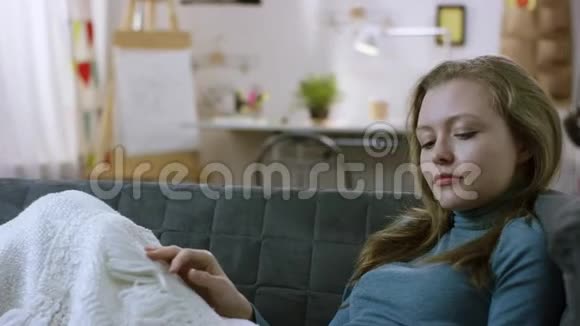 美丽的年轻女子躺在沙发上用智能手机打电话视频的预览图