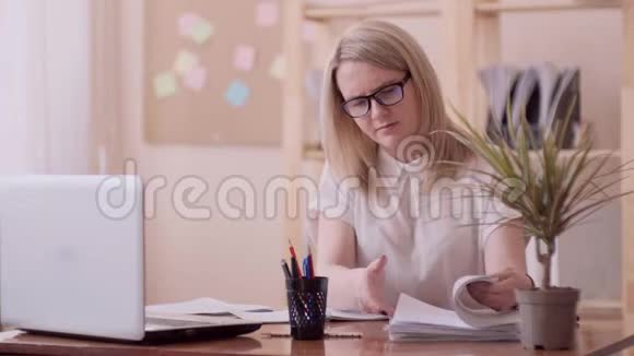 白种人外表的女孩戴着眼镜坐在办公桌后面的办公室里试图匆忙地找到视频的预览图