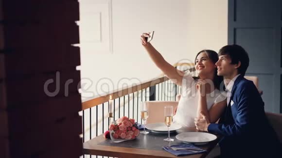 有魅力的情侣在餐厅吃晚饭时正在用智能手机自拍年轻人在微笑视频的预览图