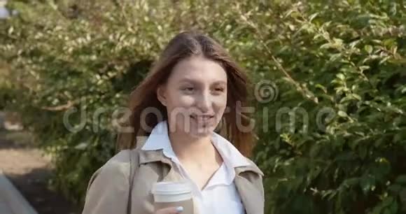 年轻迷人的商务女性走在历史悠久的绿色城市地区端着杯子喝着热咖啡看上去很漂亮视频的预览图