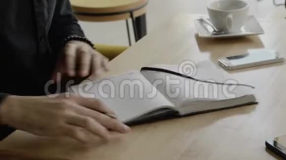 商人的手有一个人的最高视野笔和笔记本坐在咖啡馆的木桌上视频的预览图