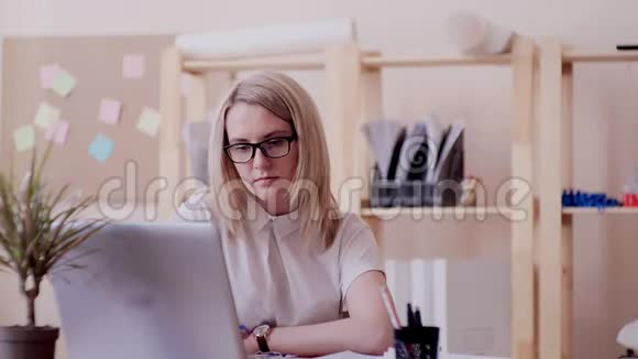 戴眼镜的白种人女孩坐在办公室手提电脑抬头向她解释视频的预览图