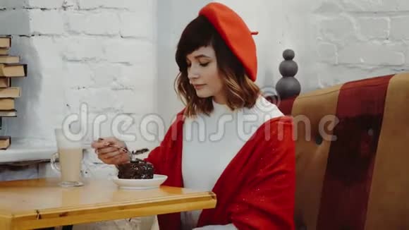 白种人的可爱女孩穿着红色贝雷帽坐在咖啡馆里在桌子上切蛋糕这是一种鸡尾酒视频的预览图