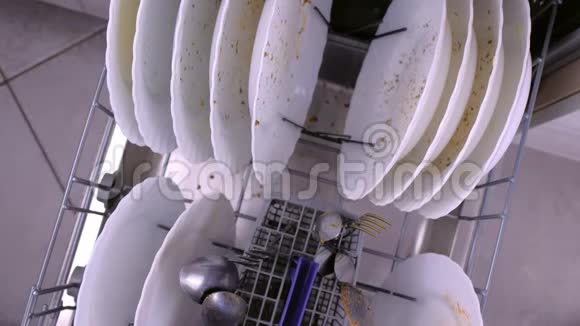 男人手把白色的脏盘子和勺子放在洗碗机的篮子里然后推它视频的预览图