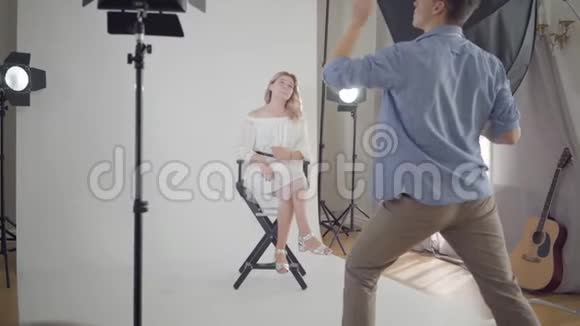 拍摄的后台男摄影师为坐在白色椅子上的迷人优雅女人拍照视频的预览图