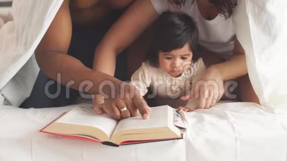 一个多种族的家庭在卧室的毯子下面读一本儿童百科全书视频的预览图