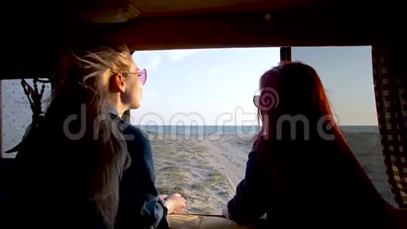 在日落时分几个年轻的女人透过汽车拖车窗口望着沙滩和大海视频的预览图