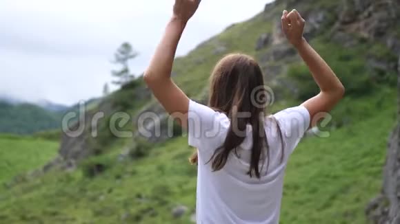 站在山顶上的漂亮女孩正在跳跃和举手慢动作视频的预览图