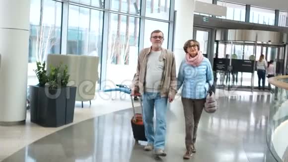 成熟的女人和男人穿过机场航站楼那个人手里拿着一个手提箱浪漫旅行情侣视频的预览图