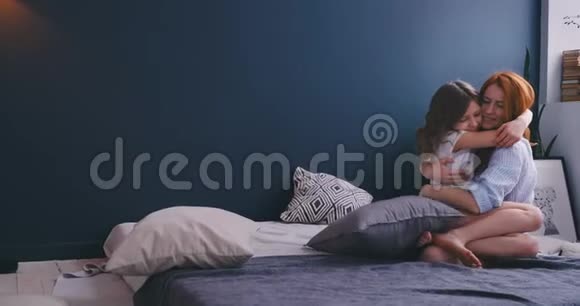 年轻的母亲红头发坐在床上抱着女儿穿着睡衣早上好亲爱的妈妈视频的预览图