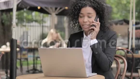 非洲女商人坐在户外咖啡厅边打电话视频的预览图