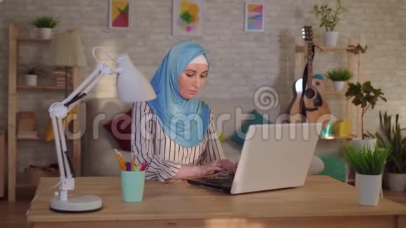 年轻的穆斯林妇女戴着头巾脸上有烧伤的伤疤在笔记本电脑上工作视频的预览图
