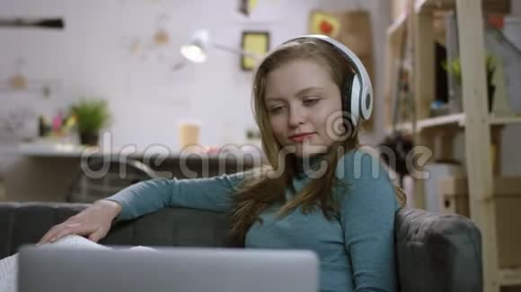 年轻女子戴着耳机在笔记本电脑上看电视节目微笑着视频的预览图