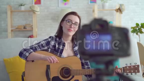 肖像年轻女性博客作者坐在沙发上手里拿着吉他在镜头前视频的预览图
