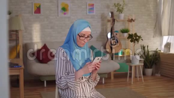 年轻的穆斯林妇女戴着头巾脸上有烧伤的伤疤她用智能手机视频的预览图