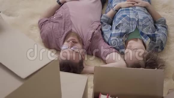 兴高采烈的年轻一家在毛茸茸的地毯上讨论公寓的内部布局已婚夫妇搬进视频的预览图