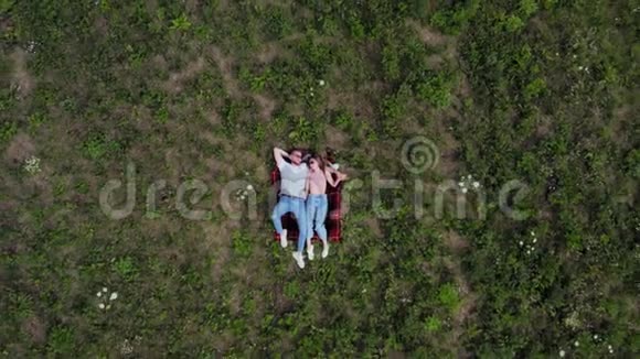 幸福的年轻夫妇躺在草地上摄像机慢慢地从他们身边飞走了从高空向下4K视频的预览图