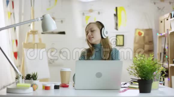 年轻漂亮的女人一边坐在桌子旁一边用手提电脑一边听音乐一边喝咖啡视频的预览图