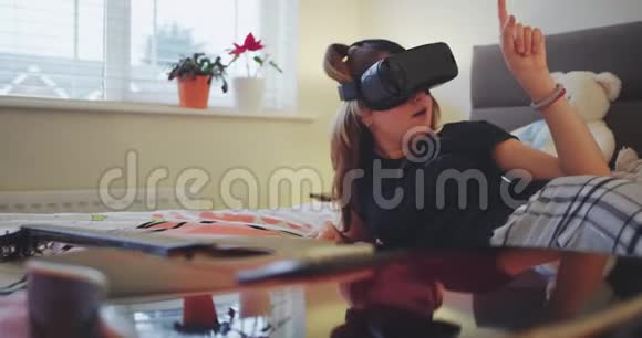 在卧室里穿着睡衣的笑容和热情的少女用虚拟现实眼镜视频的预览图