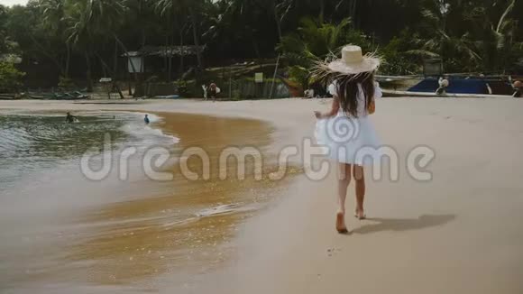 镜头跟随快乐兴奋的小57岁的女孩走在异国情调的热带海洋海滩戴着大草帽视频的预览图