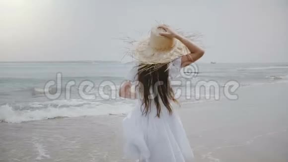 快乐美丽的5岁至7岁女孩头发飞扬戴着大草帽沿着热带异国情调的海洋海滩奔跑视频的预览图