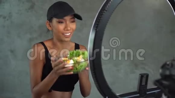 年轻的微笑女性vlogger说话时竖起大拇指同时记录她的日常健身饮食视频博客视频的预览图