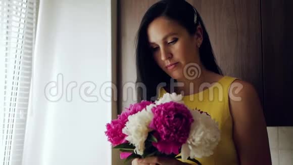 女孩嗅着花一个美丽的白人女孩把一束牡丹带到她的脸上吸入他们的气味视频的预览图