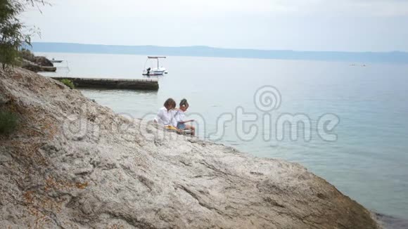 快乐的孩子一个男孩和一个女孩坐在一个岩石海岸学校友谊家庭度假视频的预览图