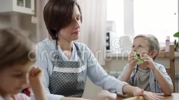 当孩子们用流动相机讲述故事时妈妈和孩子们一起在厨房的桌子上滚面团做饼干视频的预览图