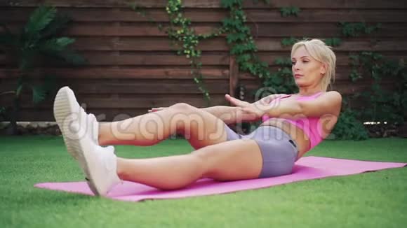 年轻的运动女子训练躺在绿草地上的腹肌视频的预览图