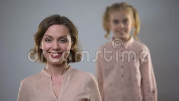年轻漂亮的女士带着一个金发女儿站在镜头后面的微笑镜头视频的预览图