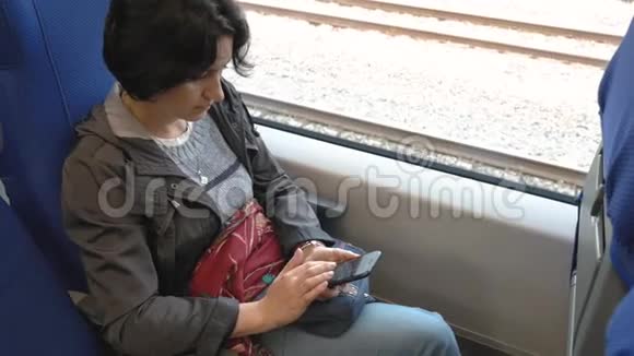 一个女人坐在火车的窗户边拿着智能手机视频的预览图