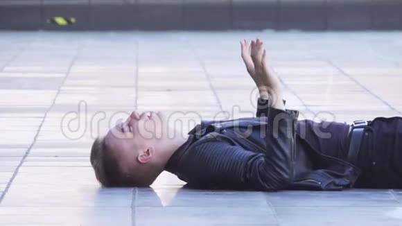穿着黑色夹克的金发小伙子躺在白色瓷砖地板上唱歌视频的预览图
