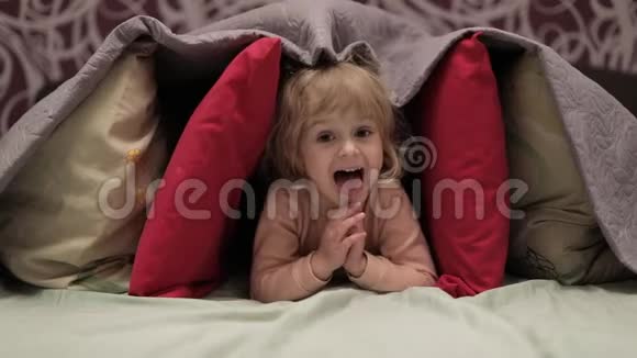 小女孩躲在床上的毯子和枕头下面藏匿地点的概念视频的预览图