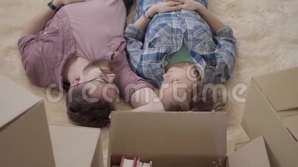 一对年轻夫妇躺在地板上有许多盒子靠近男人和女人说话躺在蓬松的地毯上已婚视频的预览图