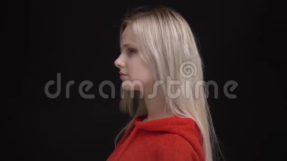 穿红色毛衣的白毛白种人年轻女孩的肖像转向照相机平静地观看黑色镜头视频的预览图