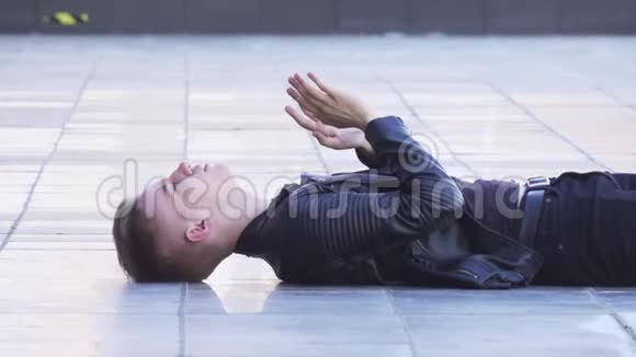 英俊的年轻白种人穿着黑色夹克躺在白色的瓷砖地板上视频的预览图