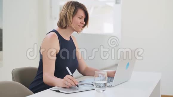 年轻的白人女性设计师使用平面笔平板电脑在笔记本电脑上工作视频的预览图
