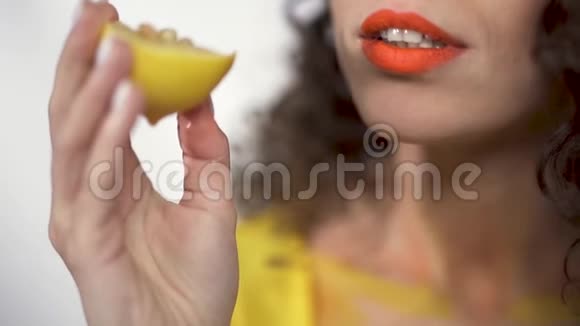 特写丰满的嘴唇与明亮的橙色口红咬酸片柠檬的乐趣慢动作视频的预览图
