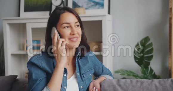 年轻女子在家里用手机说话和微笑时动作缓慢视频的预览图