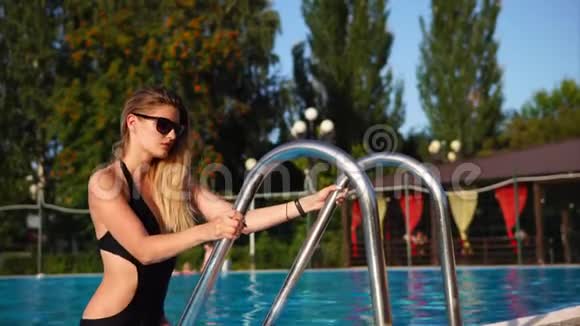 优雅的金发女郎戴着太阳镜正从大型游泳池出去视频的预览图